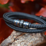Zwarte sailrope herenarmband met crematie-as in middelste rvs bedel tussen gun black rvs bedels.